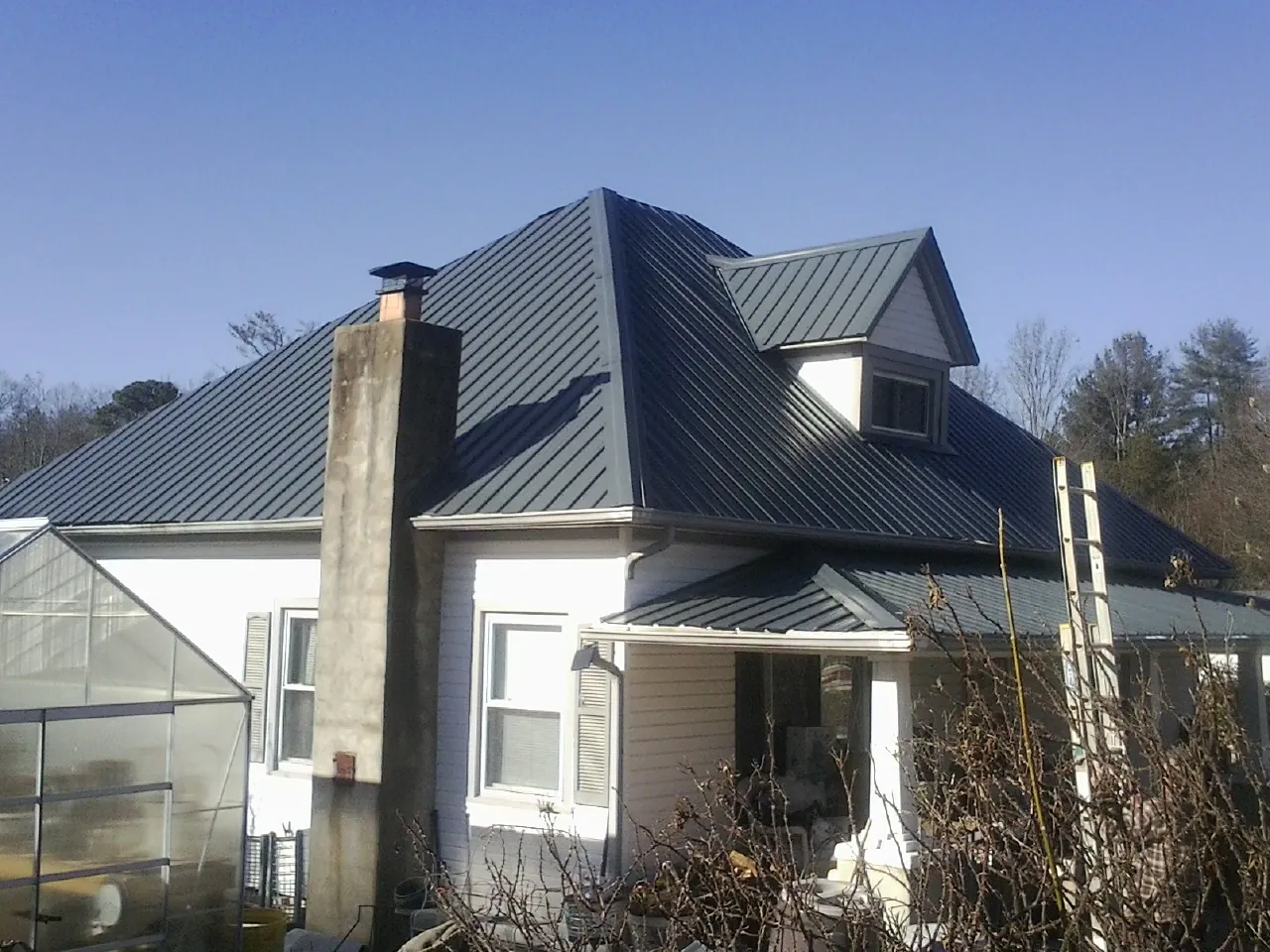 Dark blue standing seam metal roof on a white farmhouse with dormer — Slate & Tile Roof Repair by Roofing Brothers in Mill City