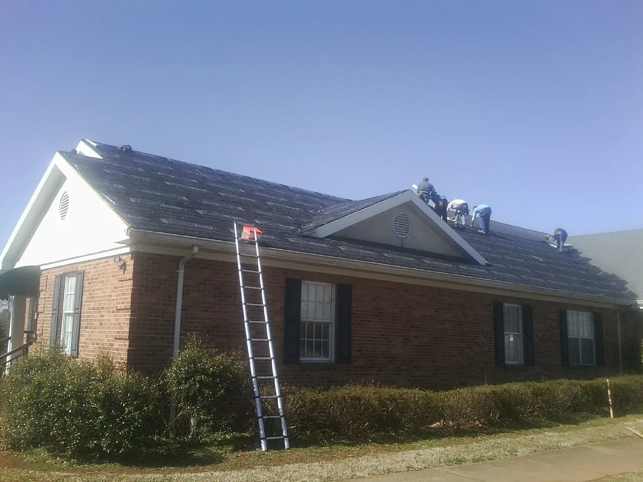 Crew tearing shingles off a brick ranch roof with a ladder set — Emergency Roof Repair work by our crew in Mill City