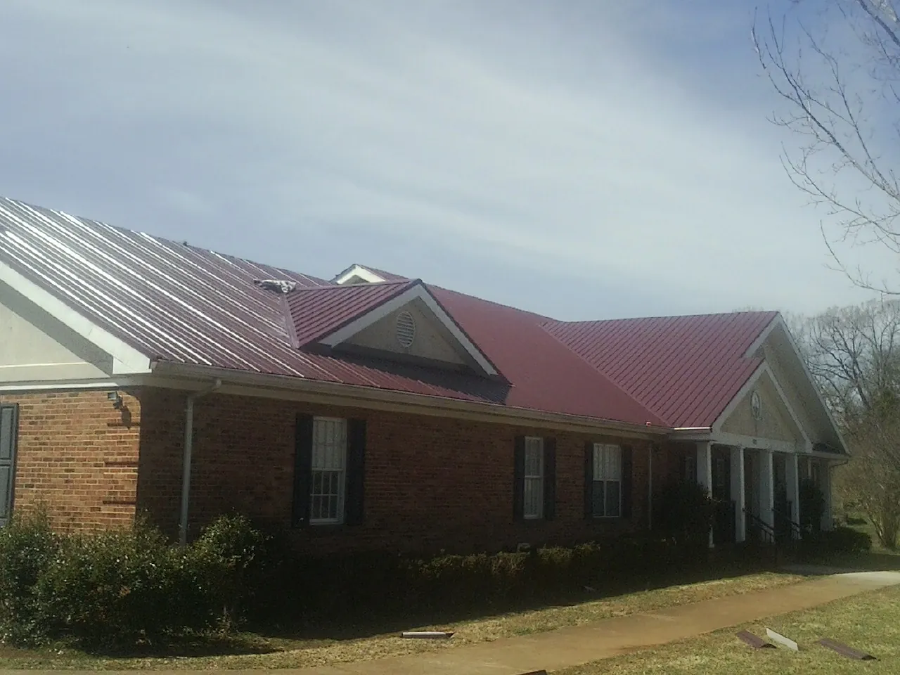 Red metal roof with gabled entries on a long brick building, from a Hail Damage Roof Repair job in Mill City