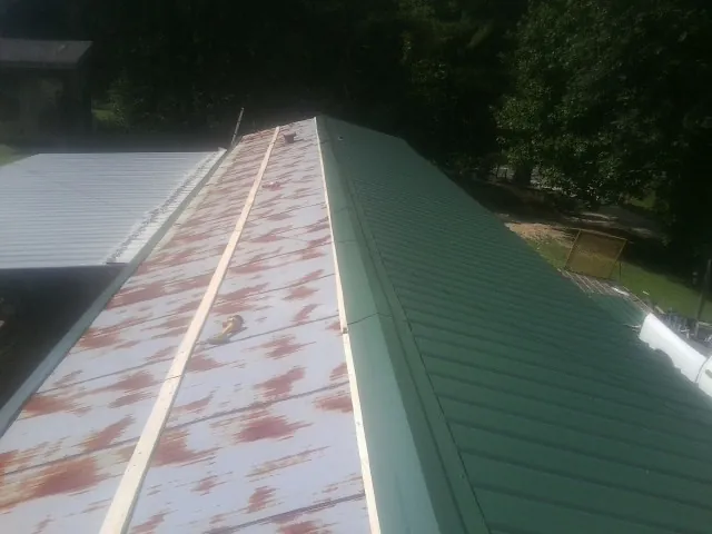 Old rusted panels beside newly installed green metal roofing — Wind Damage Roof Repair by Roofing Brothers in Mill City