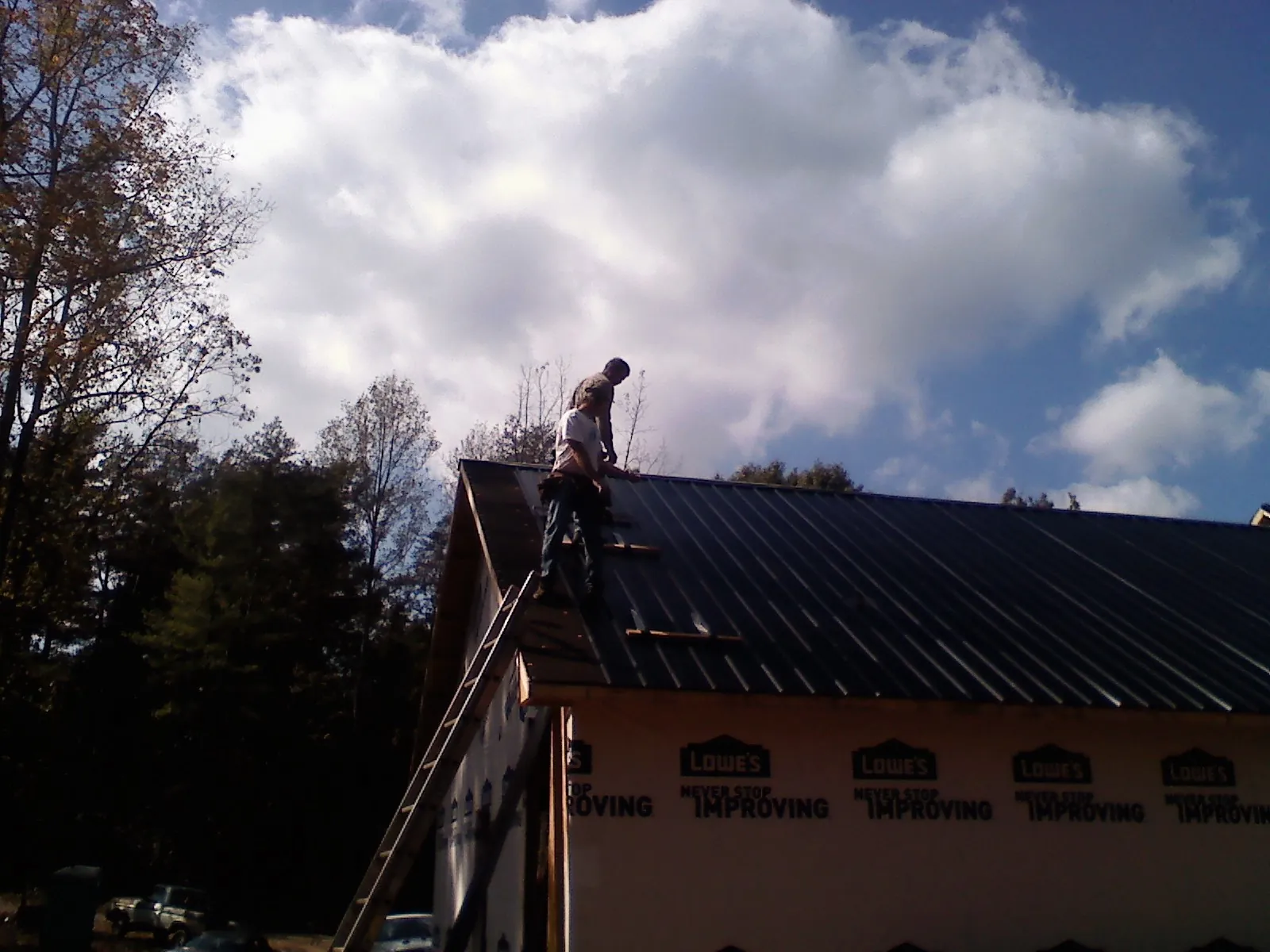Roofer fastening dark metal panels high against a cloudy sky, from a Roof Inspection job in Mill City