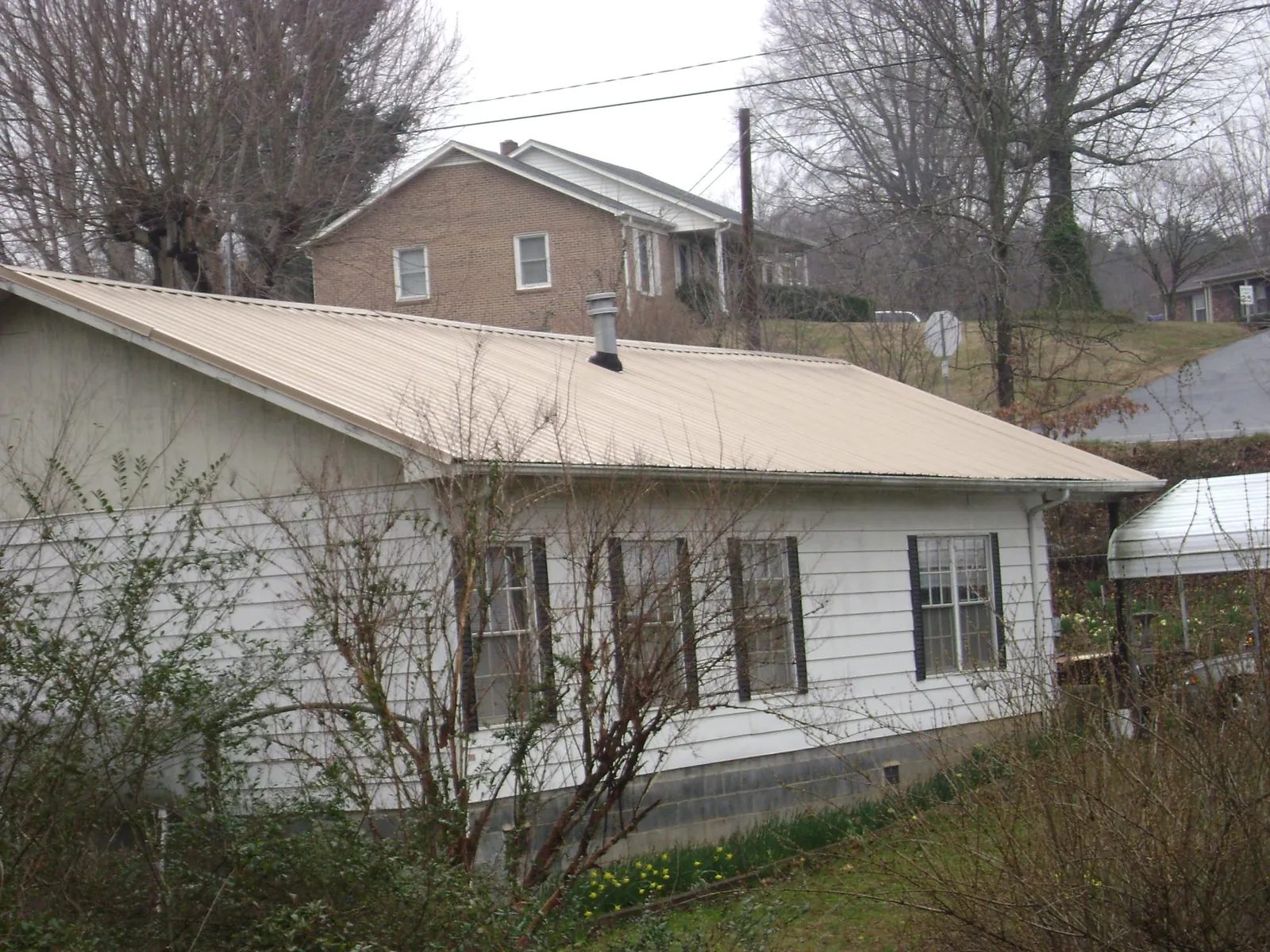 Tan metal roof on a white sided house set into a hillside — Commercial Roofing by Roofing Brothers in Mill City