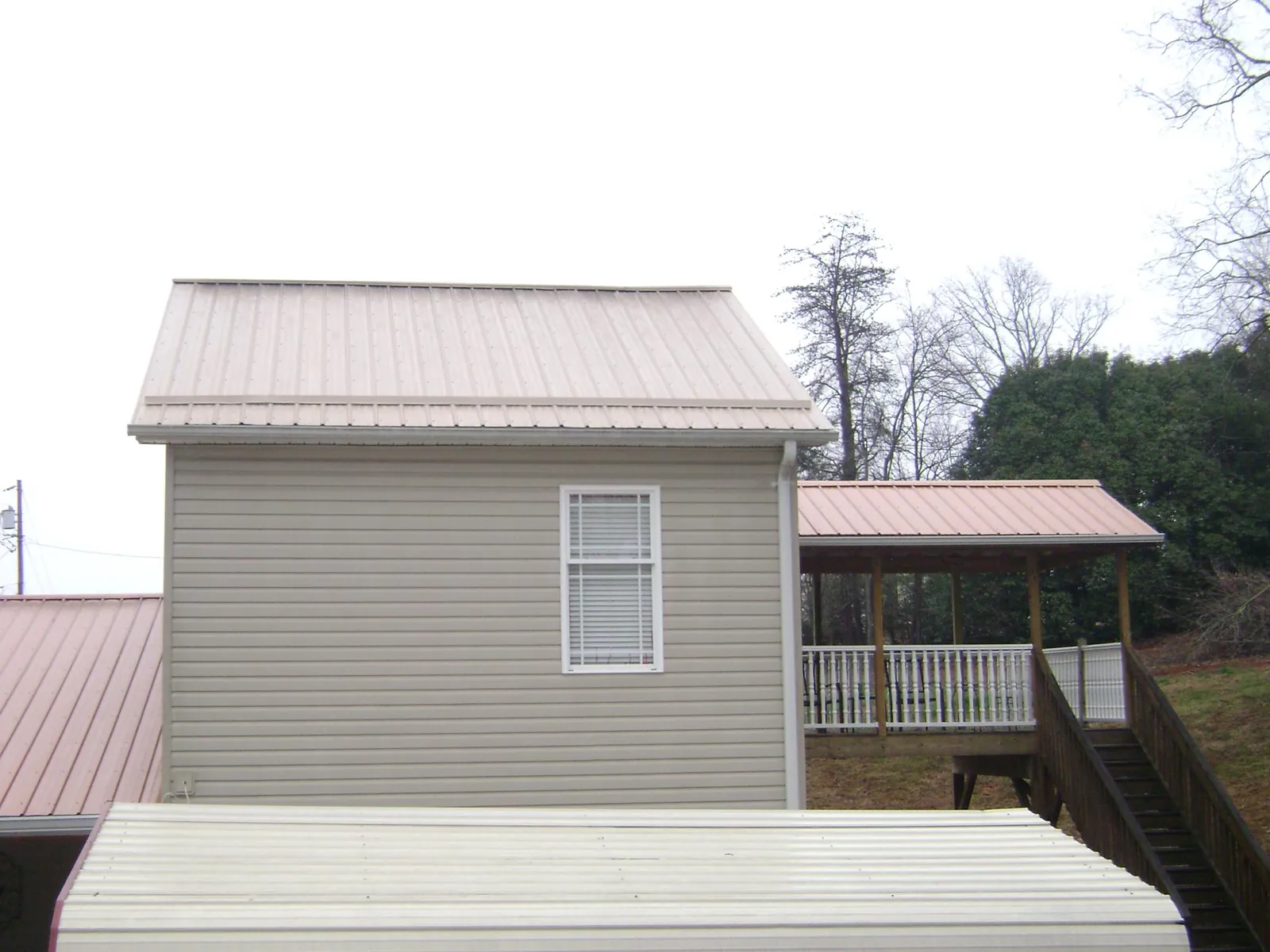 Tan metal roofs on a two story addition and attached porch, from a Roof Replacement job in Mill City