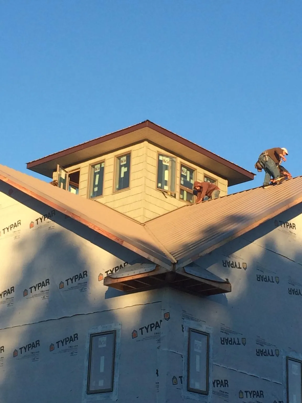 Roofers working around a rooftop cupola on a new metal roof at sunset — Roof Waterproofing in Mill City by Roofing Brothers